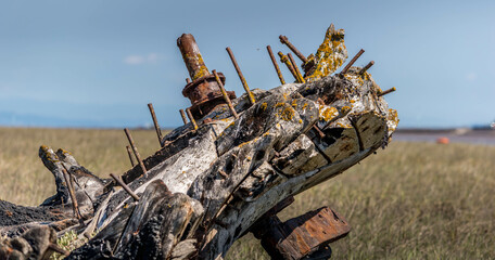 Abandoned old wooden fishing boat by river with grass and blue sky in background, shipwreck, ships graveyard, Lancashire, UK