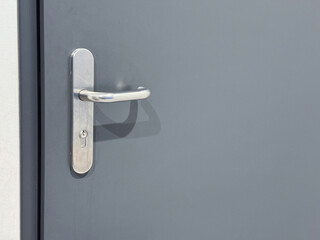 A close-up view of a silver metallic door handle on a gray door with a minimalistic design and...