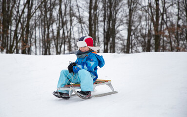 boy in winter clothes is happily sledding down a snowy slope. Winter active walks with children....