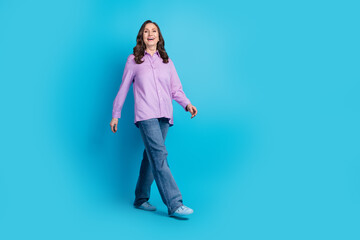 Full length photo of charming positive woman wear violet shirt walking empty space isolated blue color background