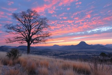 Naklejka premium Silhouette of a Tree Against a Pink and Purple Sunset Over a Mountain Range