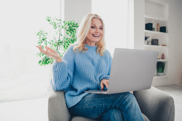 Photo of pretty aged woman speak video call laptop wear pullover free time modern apartment indoors