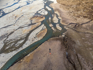 Aerial view of a river flowing through a barren landscape with a person standing on the ground.