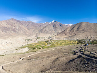 A serene valley with patches of greenery surrounded by rugged mountains under a clear sky.