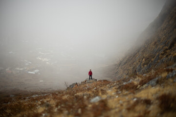 A solitary hiker stands amidst a foggy mountain landscape.