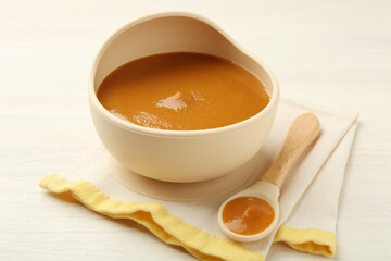 Delicious baby food in bowl and spoon on white wooden table