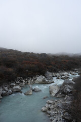 A misty river flows through rocky terrain with sparse vegetation.