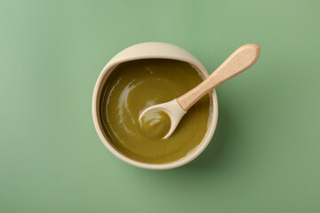 Delicious baby food with spoon in bowl on green table, top view