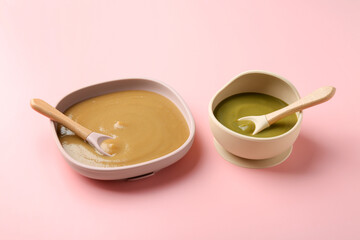 Delicious baby food and spoons in bowls on pink table