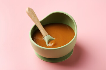 Delicious baby food with spoon in bowl on pink table