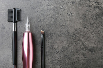 Professional permanent makeup machine and different brushes on grey background, flat lay. Space for...