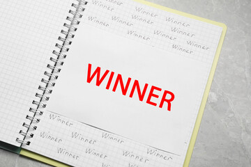 Notebook with words Winner on grey marble table, top view