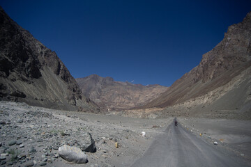 A lone traveler on a motorcycle journeys through a vast mountainous desert terrain under a clear blue sky.