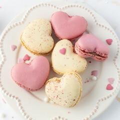 French sweet cookies macarons macaroons with color sprinkles on retro plate on marble table background. Heart shape macaron and decor.