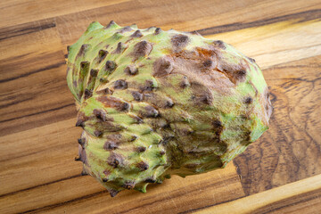 Atemoya, a tropical fuit, laying down on a wooden board, with a white background.