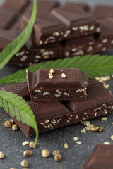 Broken dark chocolate bar with infused crushed hemp seeds on stone background. Vegan chocolate pieces and cannabis leaf and seeds closeup