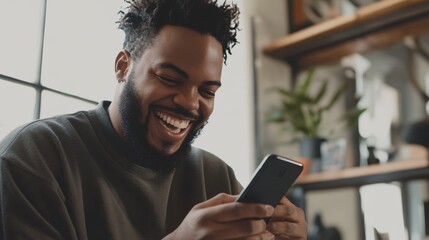 Man with a trimmed beard laughing while checking his smartphone, bright indoor light in a modern home setting
