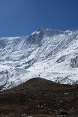Fototapeta premium A lone hiker standing on a small hill with a backdrop of majestic, snow-capped mountains.