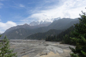 A breathtaking view of snow-capped mountains under a clear sky with a rocky, forested landscape in the foreground.