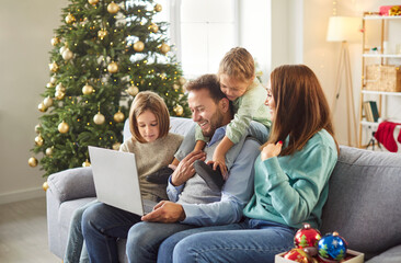 Family with children enjoys online entertainment on a laptop at home during Christmas or New Year. Together, they relax and bond during leisure time, celebrating the holiday season on the couch.