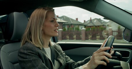 A stylish woman drives a car on a summer day. She smiles and sings