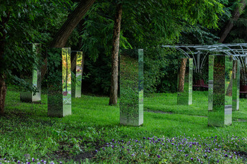 Mirror art installation in a lush green park featuring multiple tall rectangular mirrored columns...
