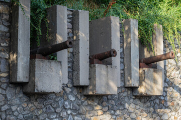 Three old rusty cannons mounted on concrete pedestals in a stone wall, surrounded by greenery. Historical monument outdoors and  defense structure. Kiev-Pechersk Fortress, Kyiv, Ukraine.
