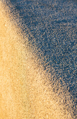 Close-up of a textured stone surface transitioning from sunlight to shadow, with a diagonal division between warm orange and cool gray tones.
