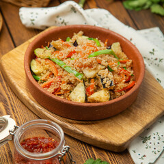 Millet porridge with eggplant, tomatoes and green onions in a plate, cafe, restaurant, on a wooden table. 
