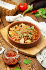 Millet porridge with eggplant, tomatoes and green onions in a plate, cafe, restaurant, on a wooden table. Vertical photo