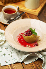 Dessert - baked apple with lingonberry in a plate, cafe, restaurant, on a wooden table. Vertical photo