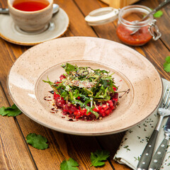Beetroot salad with arugula in a plate, cafe, restaurant, wooden table. Square photo, close-up.