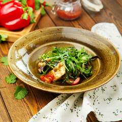 Salad of fried eggplant, arugula and cherry tomatoes in a plate, cafe, restaurant, wooden table.