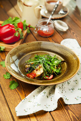 Salad of fried eggplant, arugula and cherry tomatoes in a plate, cafe, restaurant, wooden table. Vertical photo