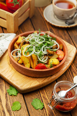 Dish of baked potato wedges with mushrooms, onions, cherry tomatoes and cilantro, in a plate, cafe, restaurant, on a wooden table. Vertical photo