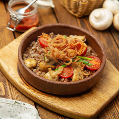 Buckwheat porridge with mushrooms, fried onions and cherry tomatoes in a plate, cafe, restaurant, on a wooden table. 