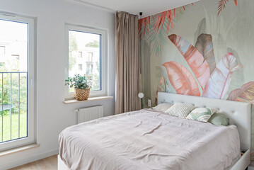 Modern bedroom with textured wallpaper with pattern of leaves. Design interior of room with pillow and comfortable bed. New apartment. Stylish house.	