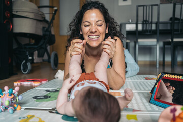 Mother lying on floor playing with baby daughter at home. Happy mother playing with her baby...