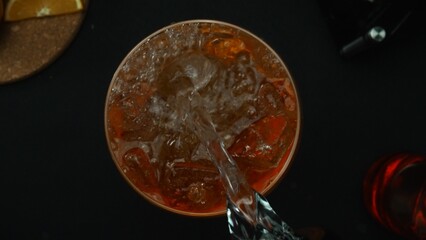 Macrography, experience the art of mixing a Negroni cocktail from a top-down perspective, adorned with a fresh vibrant orange slice, all against a dramatic black background. Top down view. Comestible.