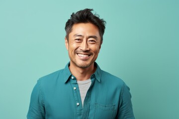 Fototapeta premium Portrait of a grinning asian man in his 40s donning a trendy cropped top in front of soft teal background