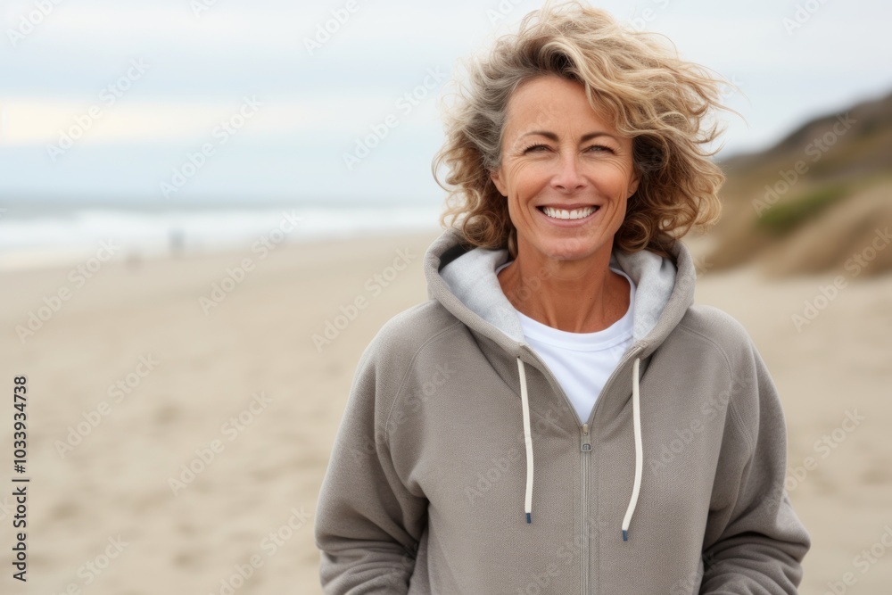 Wall mural Portrait of a happy woman in her 50s wearing a zip-up fleece hoodie isolated in sandy beach background