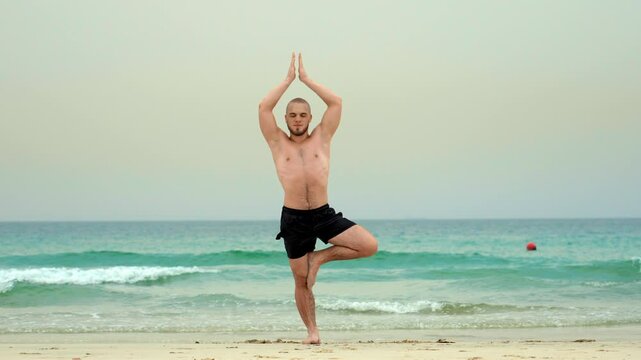 man doing yoga on the beach by the sea