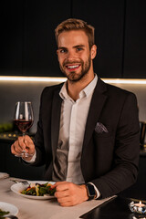 Vertical portrait of handsome young man with glass of wine indoors. Successful businessman ceo boss tasting alcohol at home, restaurant. First date, birthday celebration