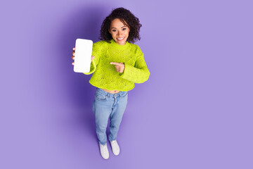 Photo of american young funky girl in green sweater finger pointing smartphone display online product isolated on purple color background