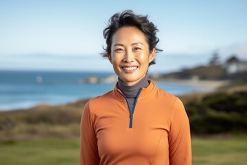 Portrait of a grinning asian woman in her 40s wearing a breathable golf polo isolated in calm bay background