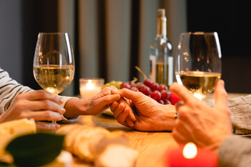 Close up cropped shot of the table during romantic dinner with lover`s hands with glasses of wine and food. Love and relationship, dating concept. Anniversary, proposal, Valentine`s Day celebration
