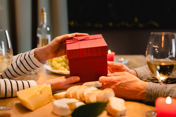 Close up shot of happy couple`s hands sharing anniversary or St. Valentines present during romantic dinner. Red gift box. Gift receiving - love language. Christmas and New Year