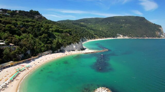 Low aerial reveal of Spiaggia del Frate and Urbani beach. Sirolo village on cliff view. Riviera del Conero Marche Italy. Turquoise Adriatic sea. 4K drone flight. Scenic coastline rotation.