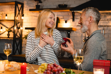 Mature caucasian man proposing his girlfriend during romantic date in the kitchen. Marriage, engagement, ring for wedding. Present gift on Valentine`s Day