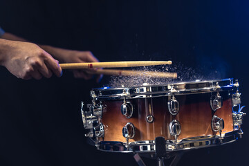 Drum sticks hitting snare drum with splashing water on black background.